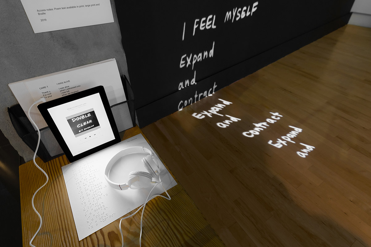 Image of headphones, projected text, and an iPad on a wooden bench, available to share poetry and artwork by E.T. Russian