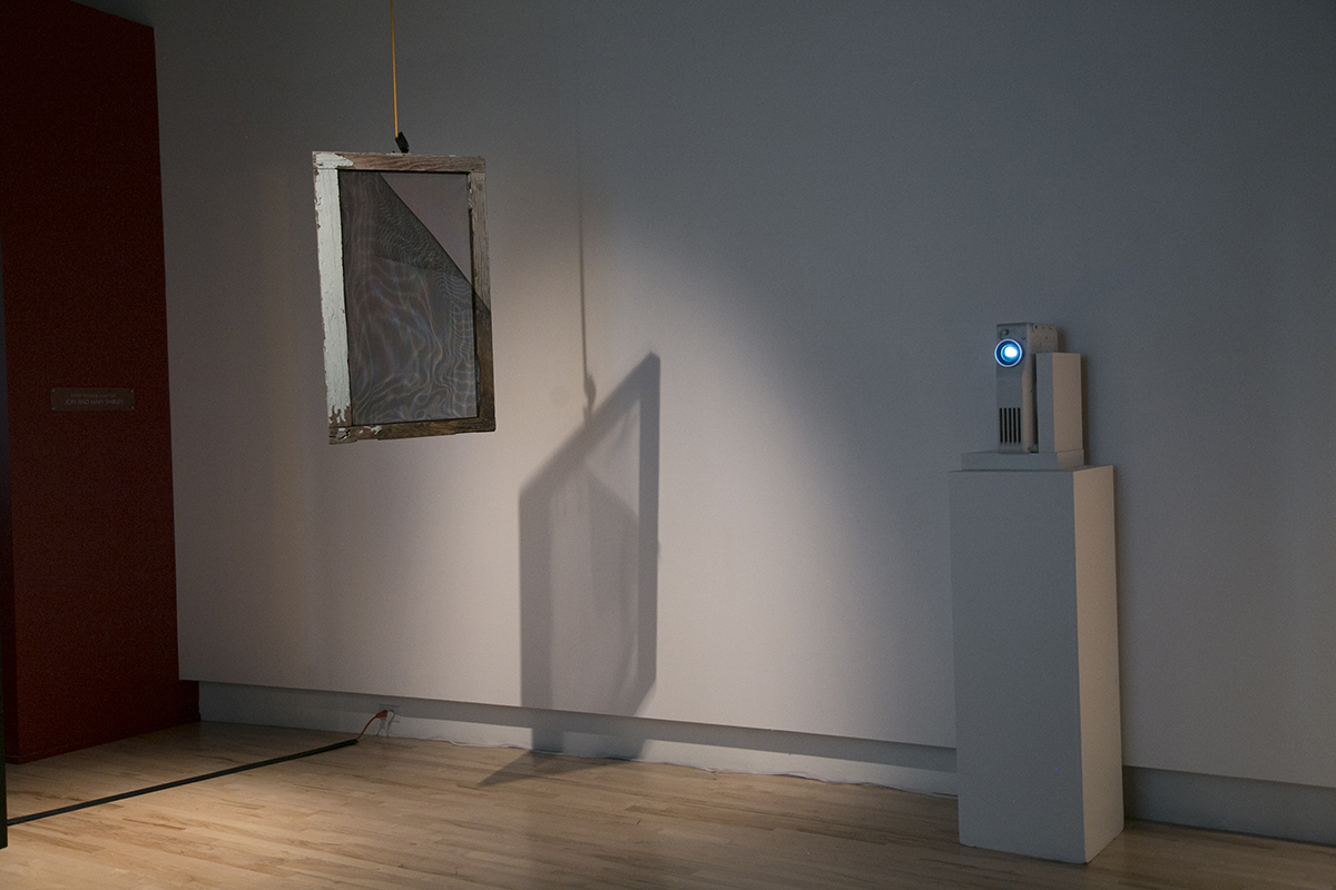 Image of a projector next to an artwork by Christopher Paul Jordan, featuring a window with white paint and a peeling screen.