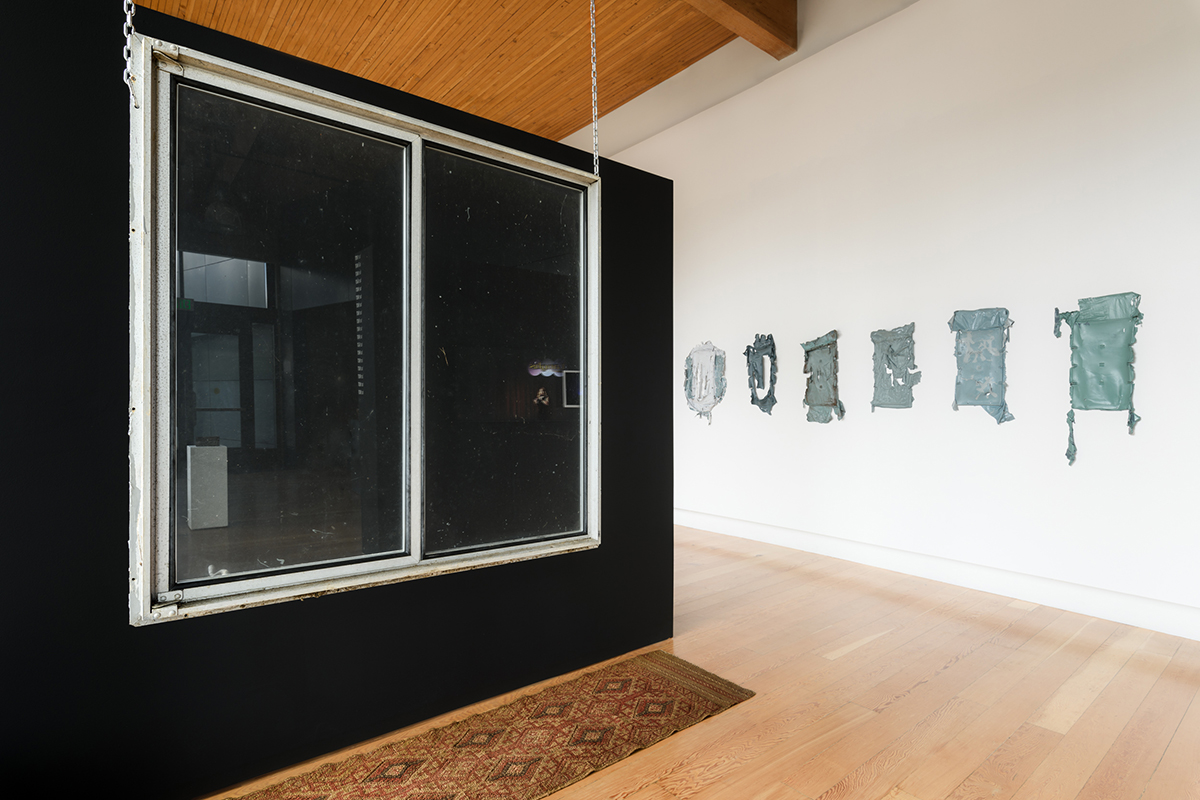 Artworks by Khadija Ann Tarver and Philippe Hyojung Kim. Window suspended near black wall with rug, 6 gray/green paintings. 
