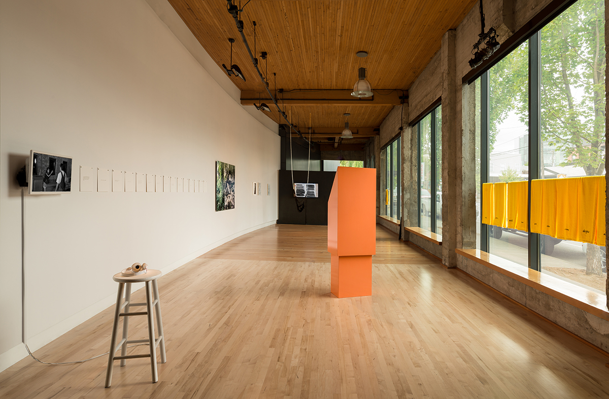 Image of artworks in Hedreen Gallery, including artworks with coral color pedestal and yellow towels in the foreground. 