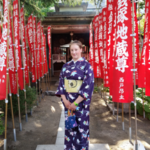 Teri wearing a violet kimono standing in front of red flags