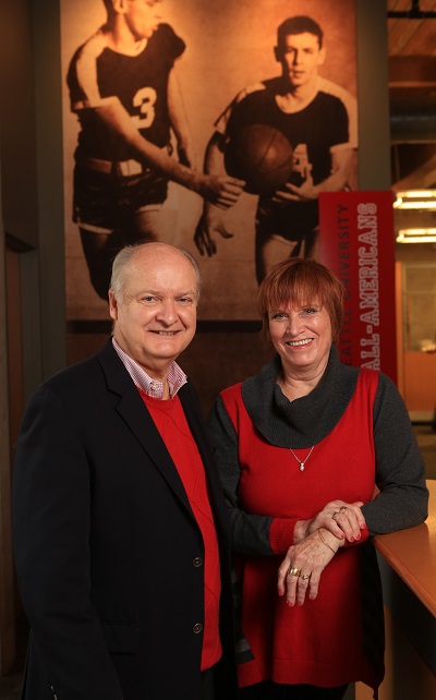 John and Diane Dougherty standing in front of a Redhawks football photo.