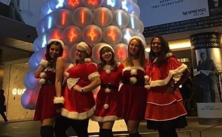 Nina and three friends stand in front of a Christmas tree in Santa outfits.