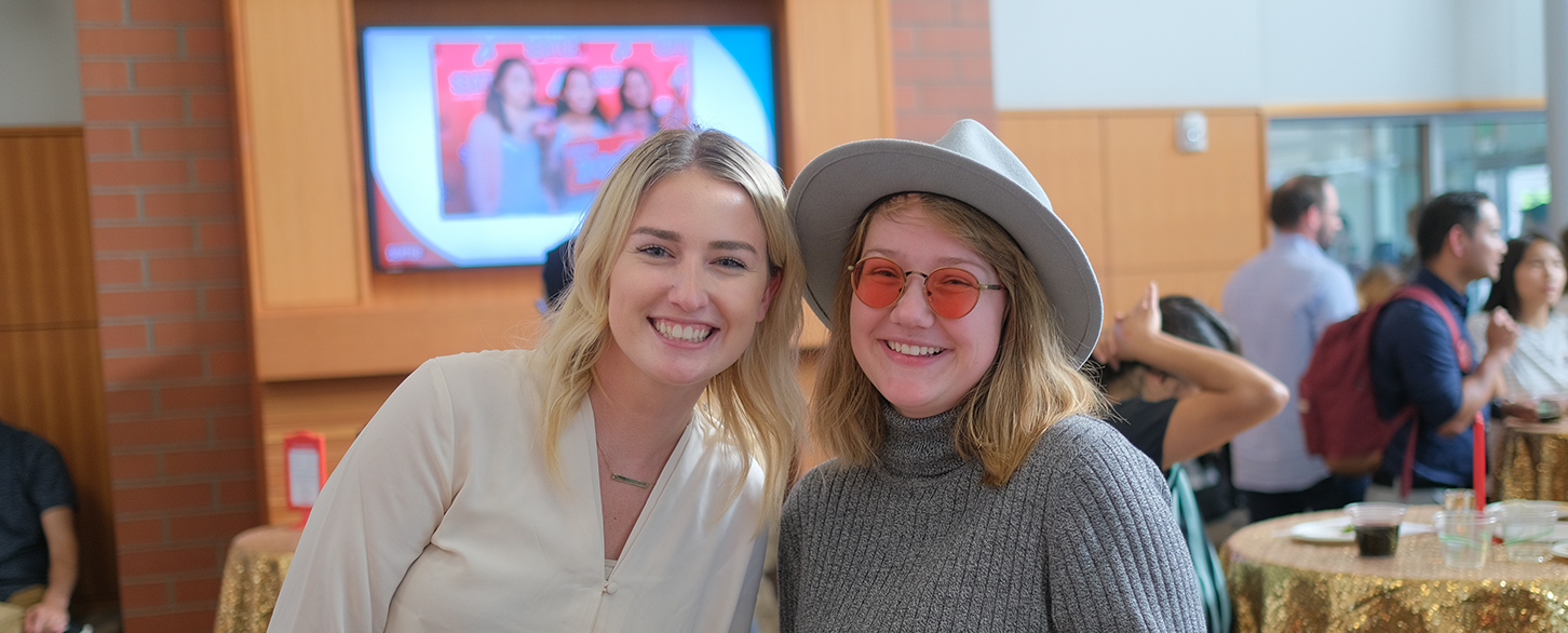 Two recent GOLD alums smile during an event in a building on campus