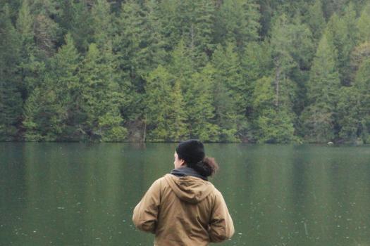 A student looks out over a lake surrounded by evergreen trees in a reflective moment on Outdoor Retreat.