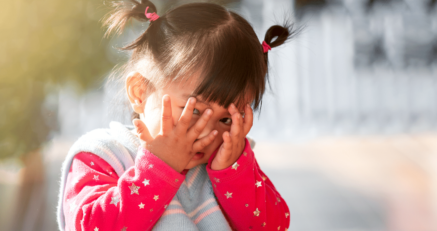 A child with pigtails covers their face in a game of peek-a-boo.