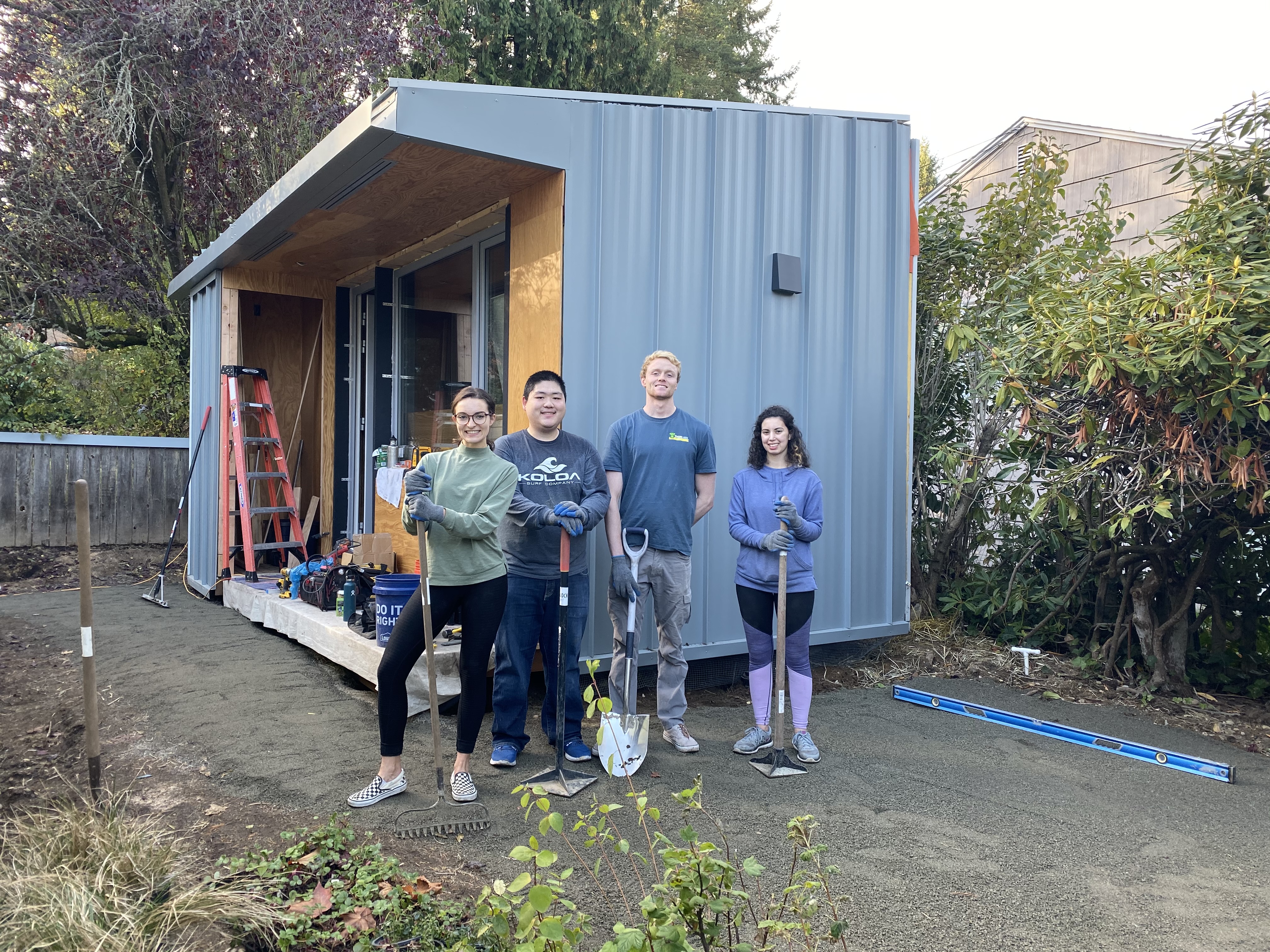 4 SU students post in front of a blue tinyhouse that they helped build in a backyard