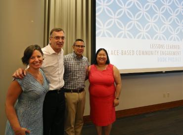 four colleagues stand in front of a projected image for the lessons from place-based community engagement book project
