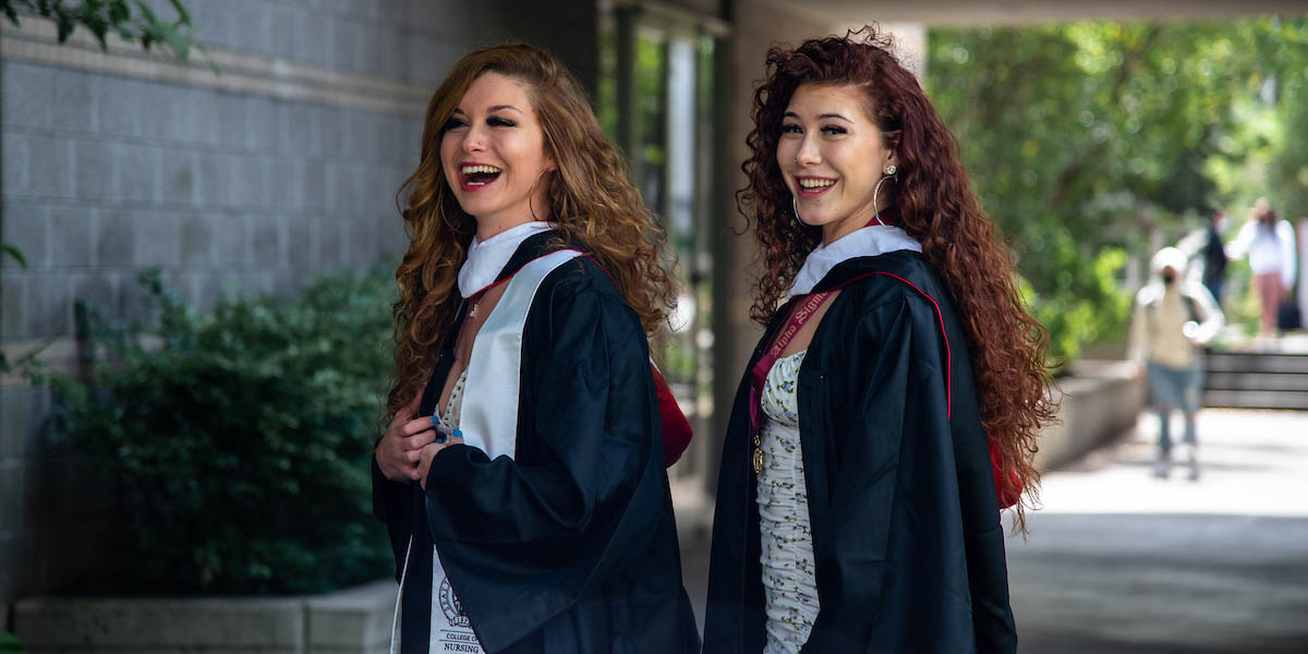 Amber Rodriguez-Munoz and Eva Rodriguez posing on campus in their graduation gowns.