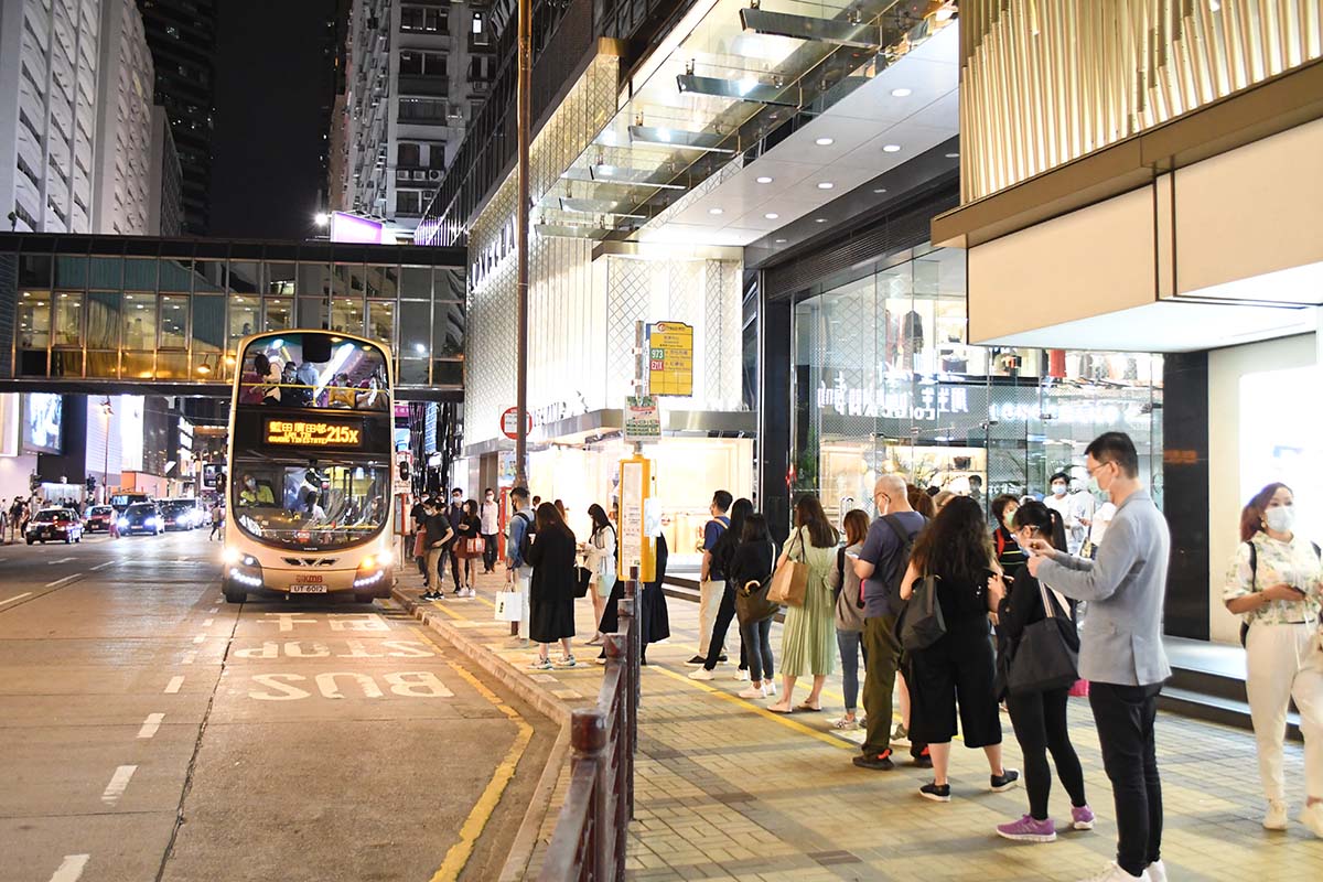 photograph of a double decker bus in a city at night with a line of people waiting 