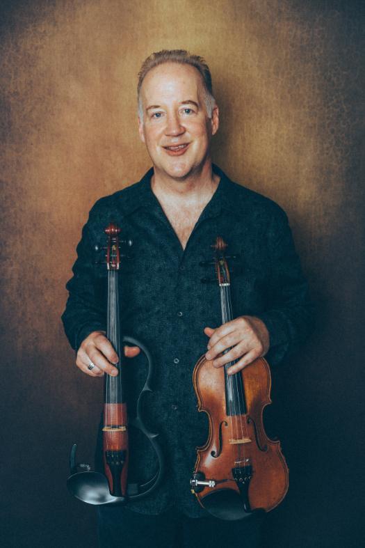 Middle aged man smiling and holding two different violins