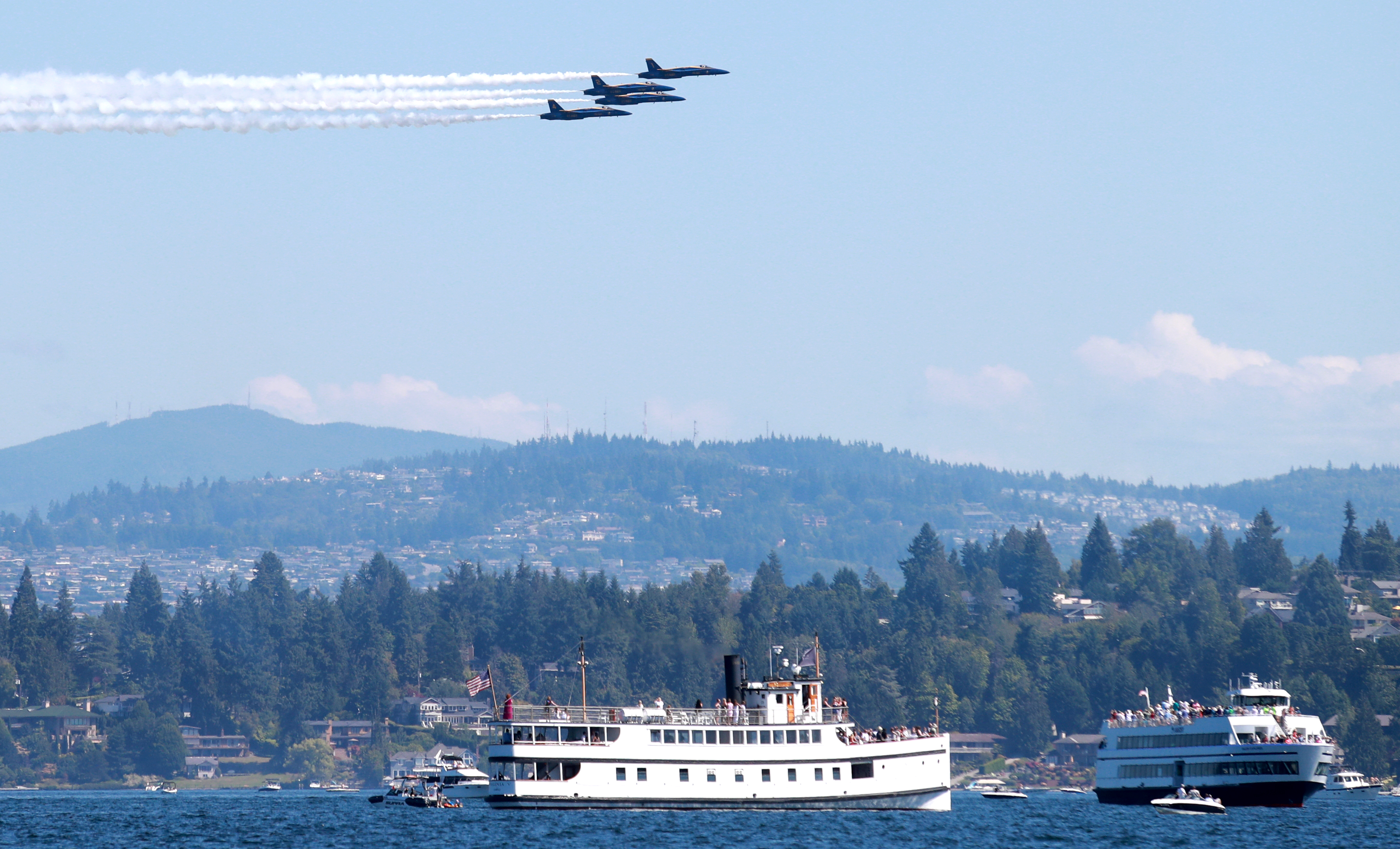 Two ferries sailing on a sunny day with three Blue Angel jets flying above