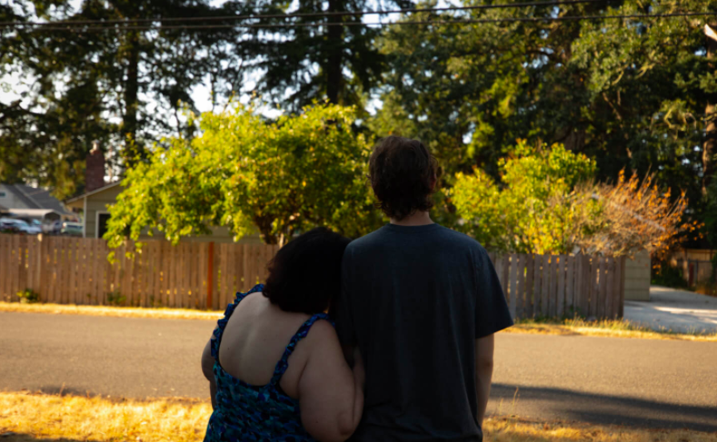 A mother and son stand together, their backs facing the camera