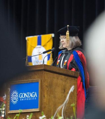 Dr. Patricia O'Connell Killen in Ph.D. Regalia standing at a podium during Commencement