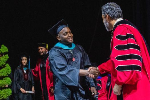 Student on stage with degree and shaking President's hand.