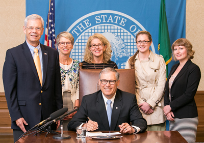 2 SU law students standing by Gov. Jay Inslee as he signs a bill