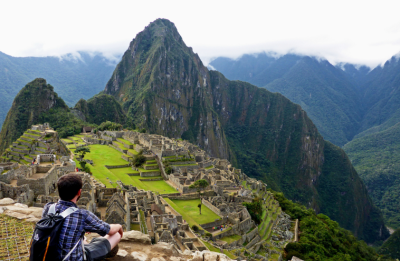 back of man sitting on an edge facing Machu Picchu