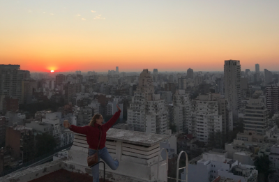 woman jumping with glee on a roof top with the sunset in the background