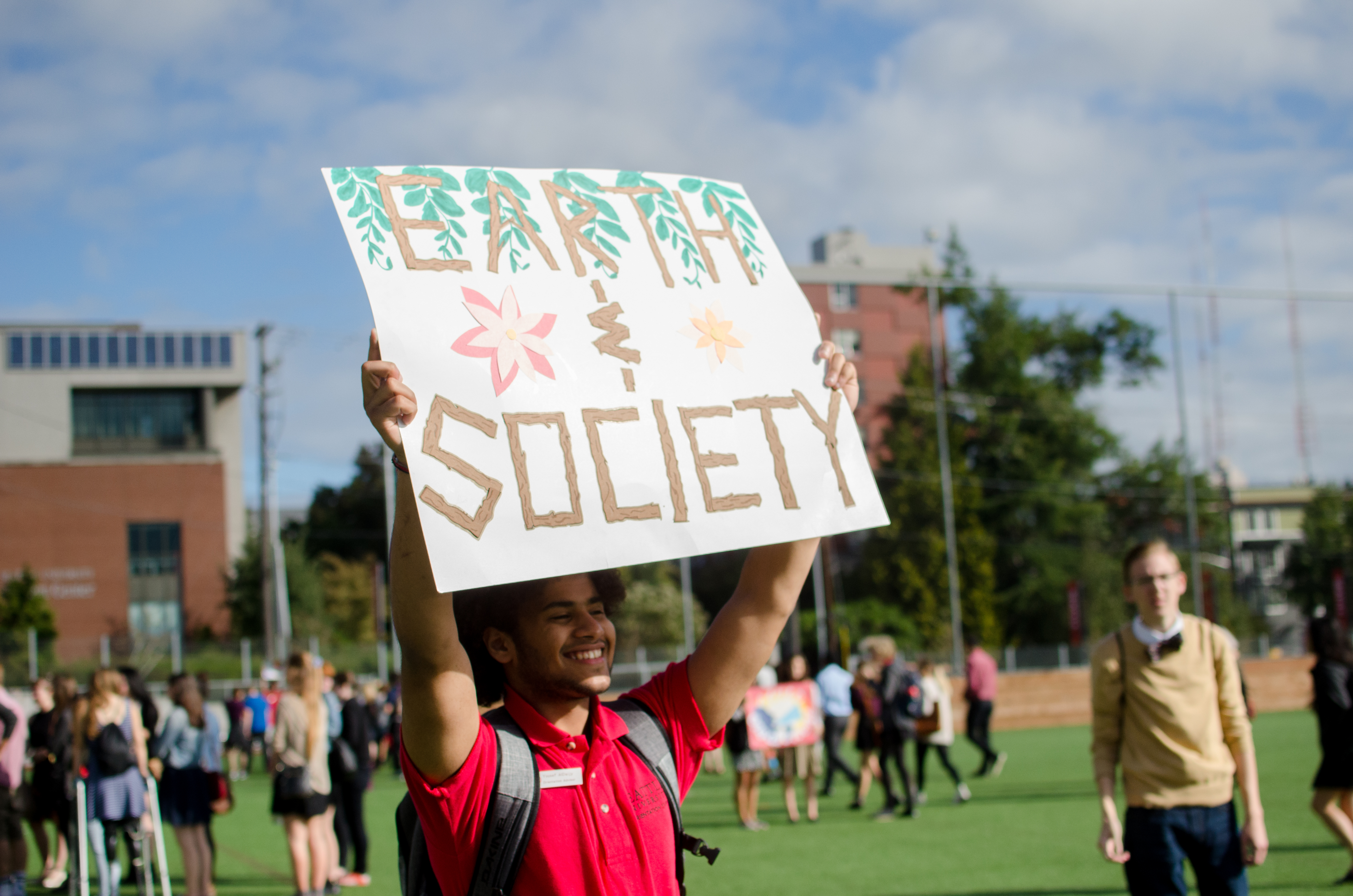 Student wearing SeattleU clothes and holding a sign that says Earth and Society.