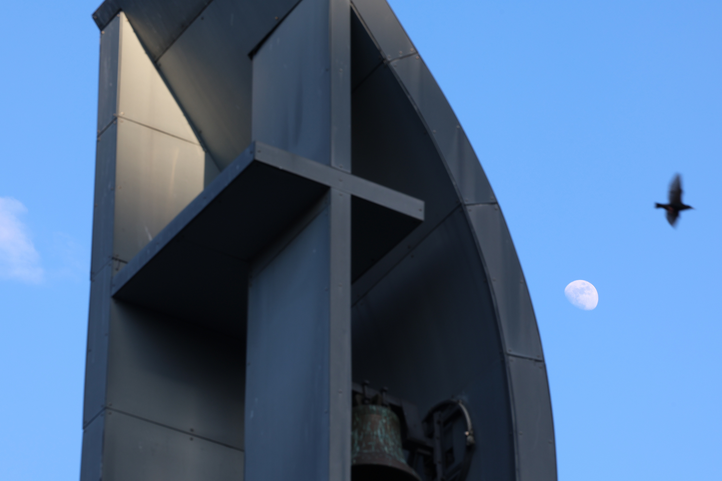 closeup of bell tower with a moon and flying bird