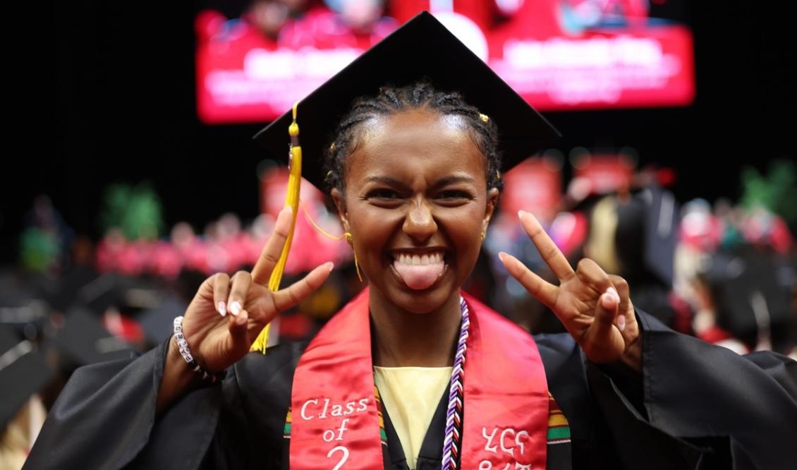 UG Commencement student with peace sign.jpeg