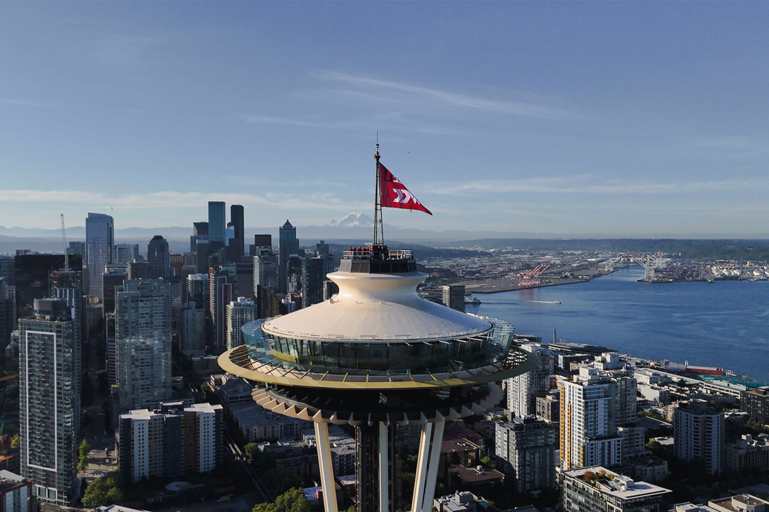 A photo of the Space Needle with the SU and WCC logo, flag on top of Space Needle