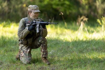 Cadet in Army greens kneeling outside weapon