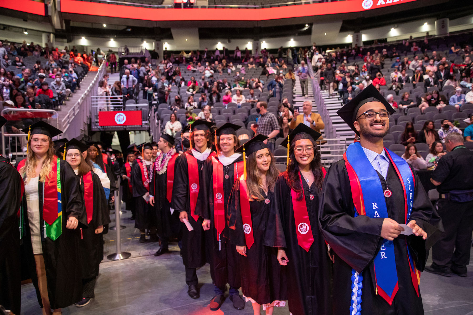 Seattle U grads walk in procession into the arena as audience members fill the seats.
