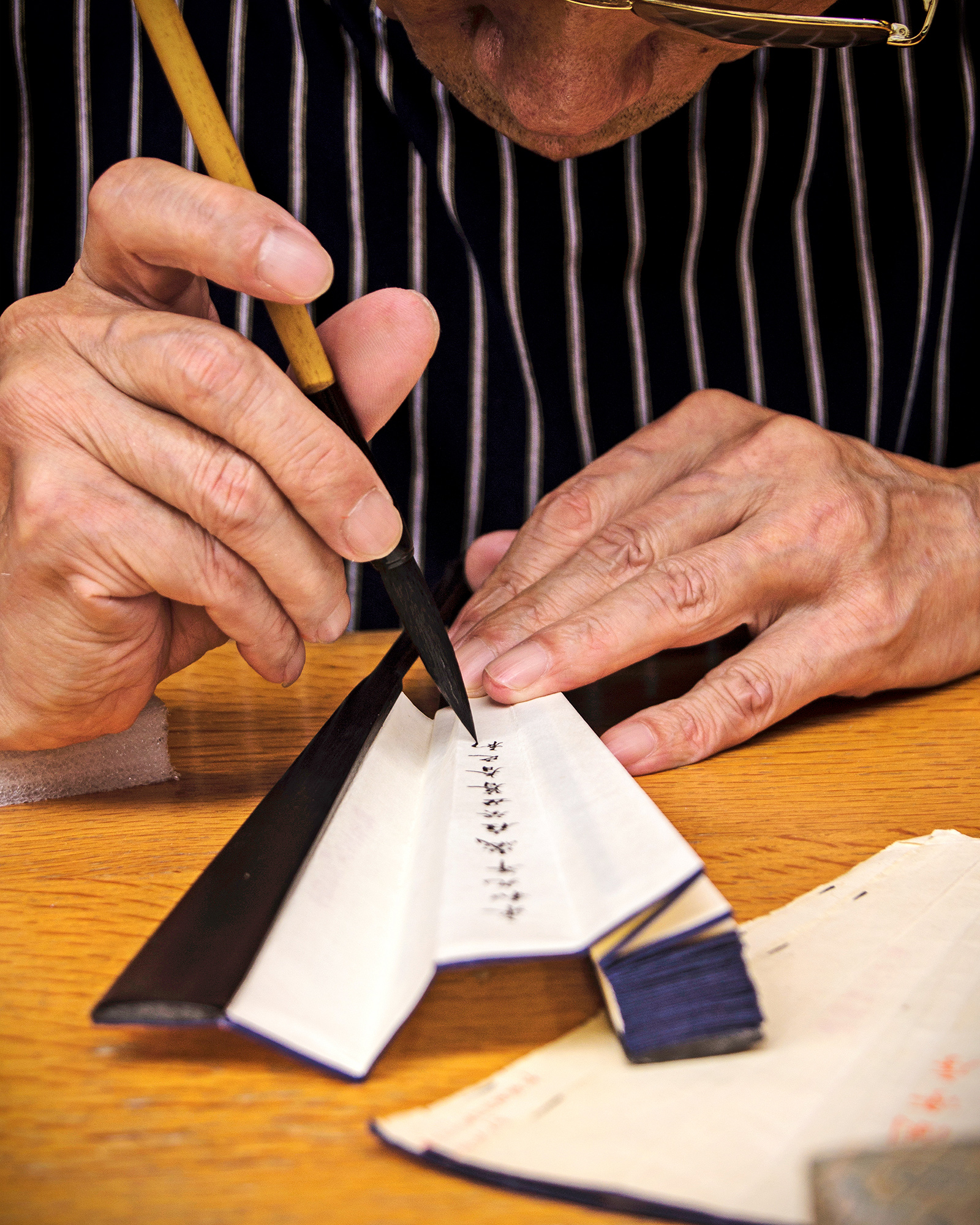 close up of man writing characters with a brush and ink on the folds of a paper fan