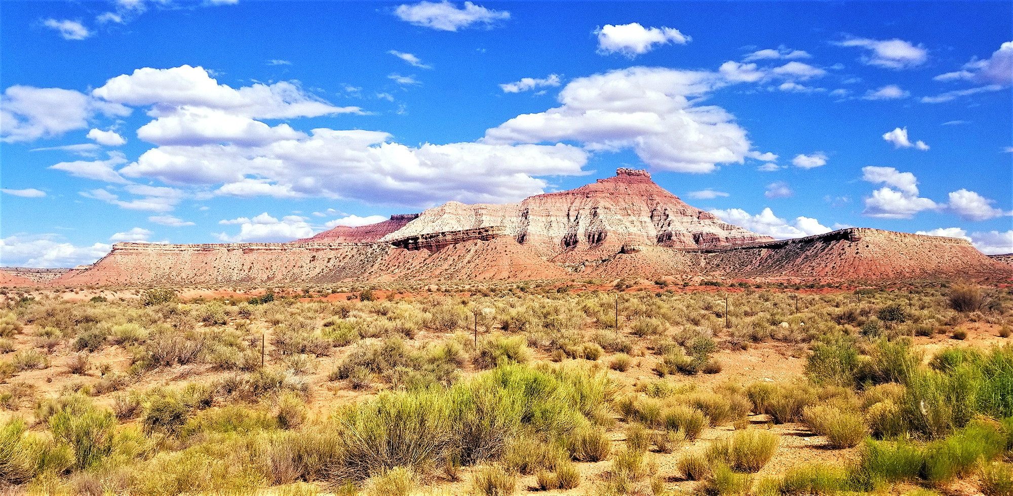Utah landscape of desert brush, mountain buttes, and a blue sky with puffy white clouds