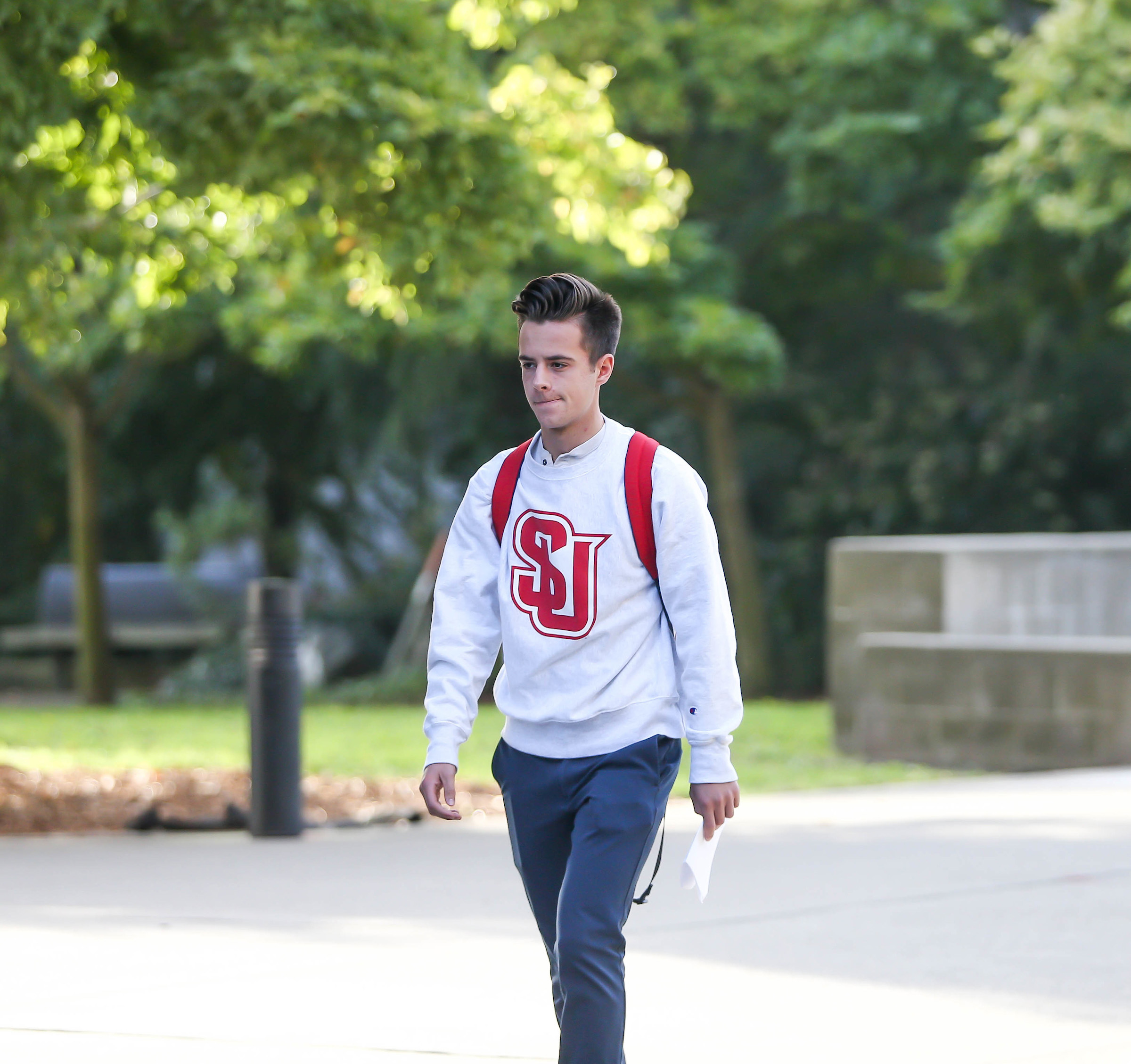 Student wearing SU sweatshirt walking through campus.