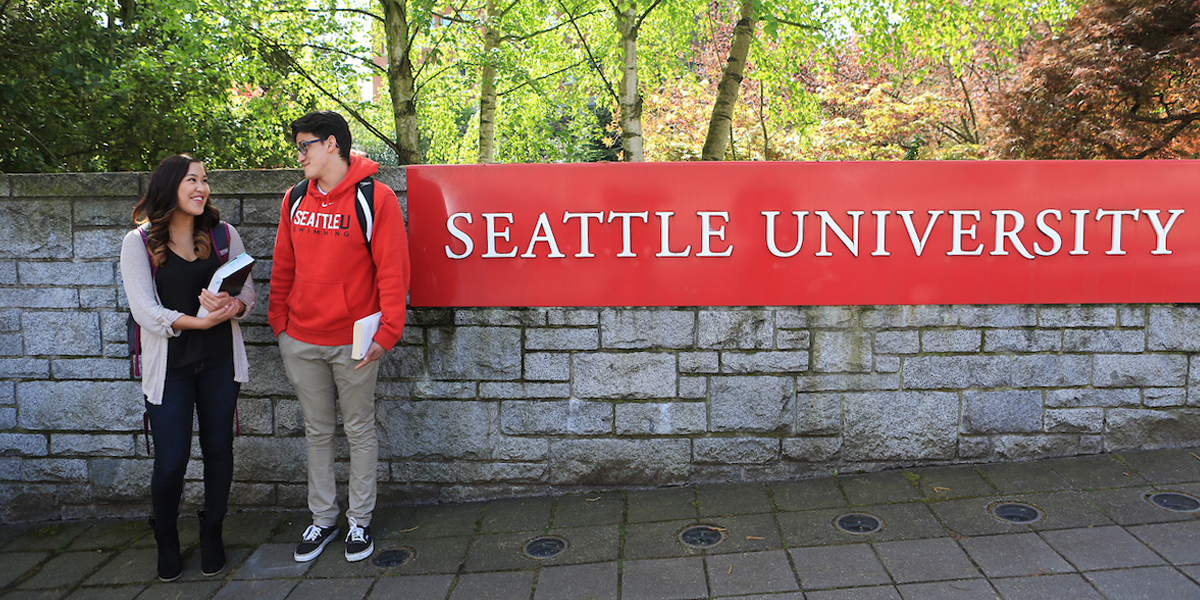 Two students stand to left of campus signage that reads "Seattle University"