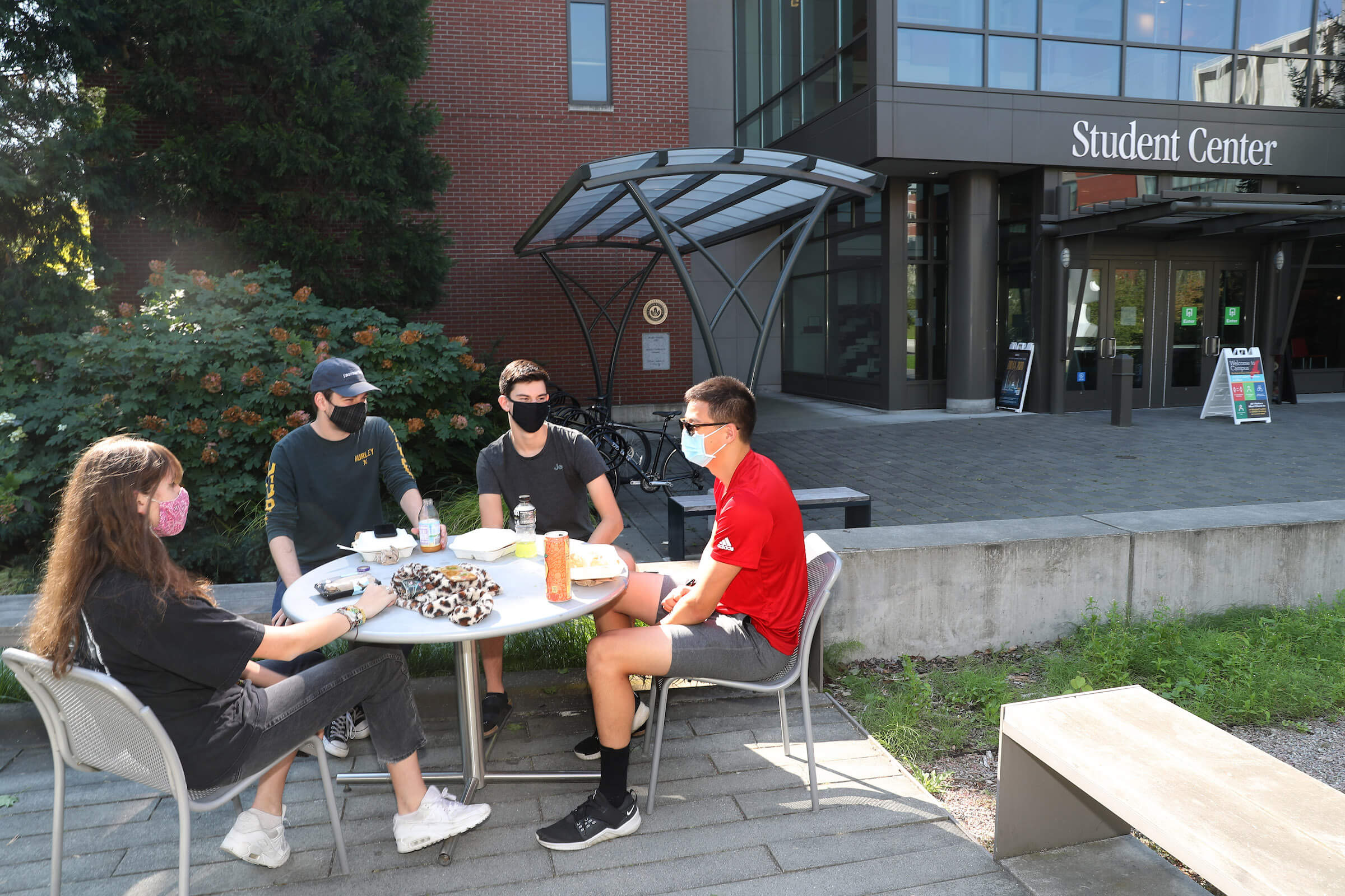 Photo on right features four students sitting at an outdoor table on campus while wearing face coverings.