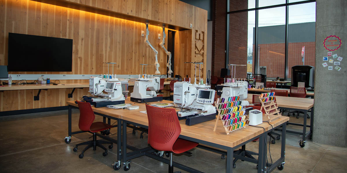Interior image of a section of the Billodue Makerspace at Seattle University. View of sewing machines, spools of thread, a flat screen TV and a 3D printer.