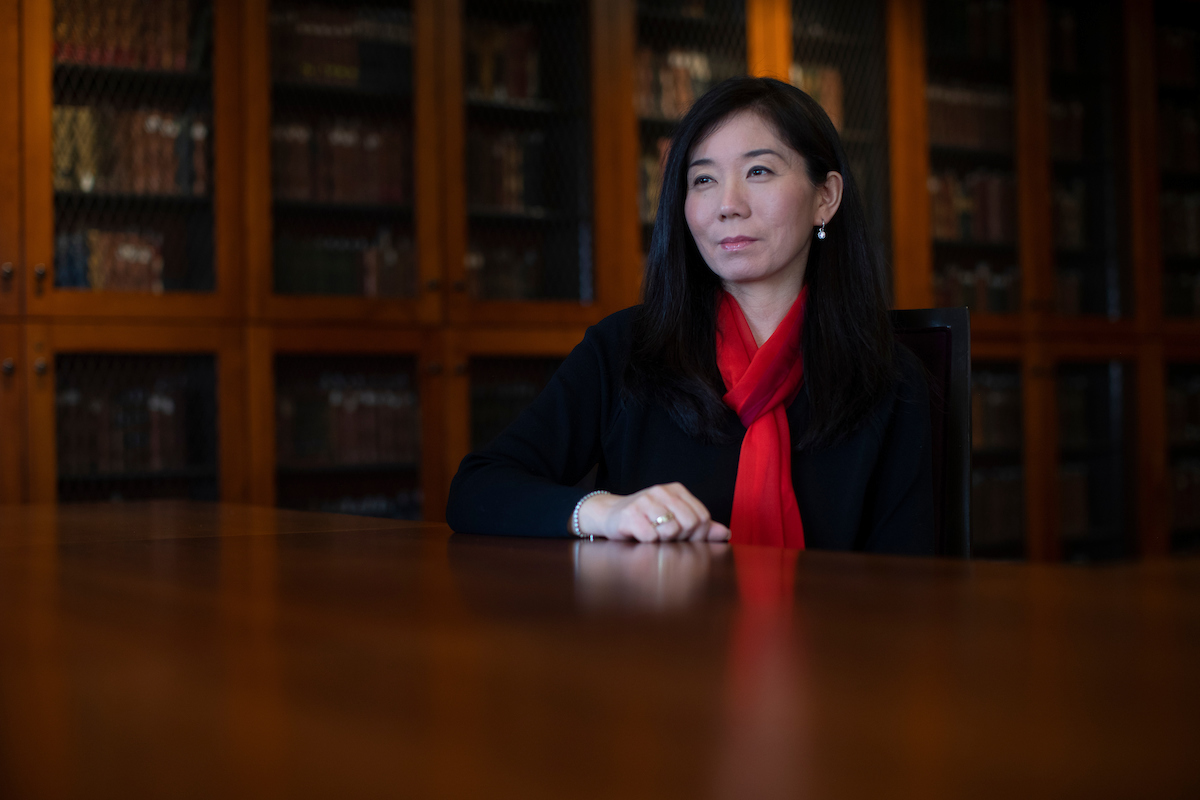 College of Nursing Assistant Professor Kumhee Ro sits inside a library room lined with books. 
