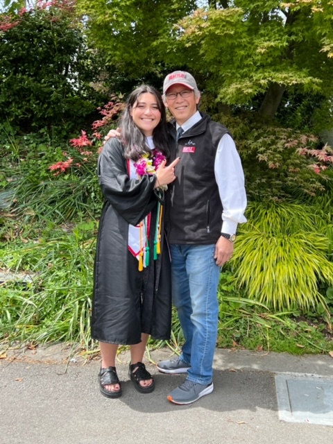 Allison wearing graduation robe standing next to her father
