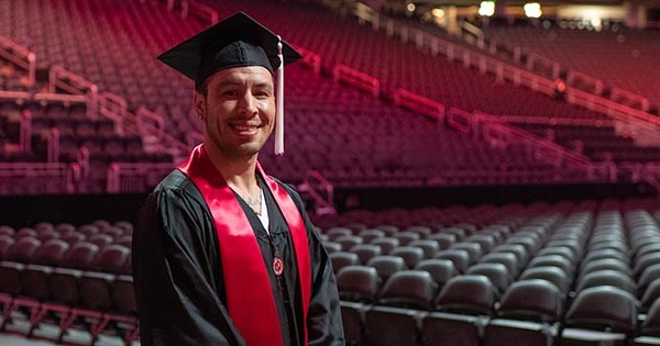 Anthonny standing and smiling in his black cap and gown at SU Commencement ceremony.