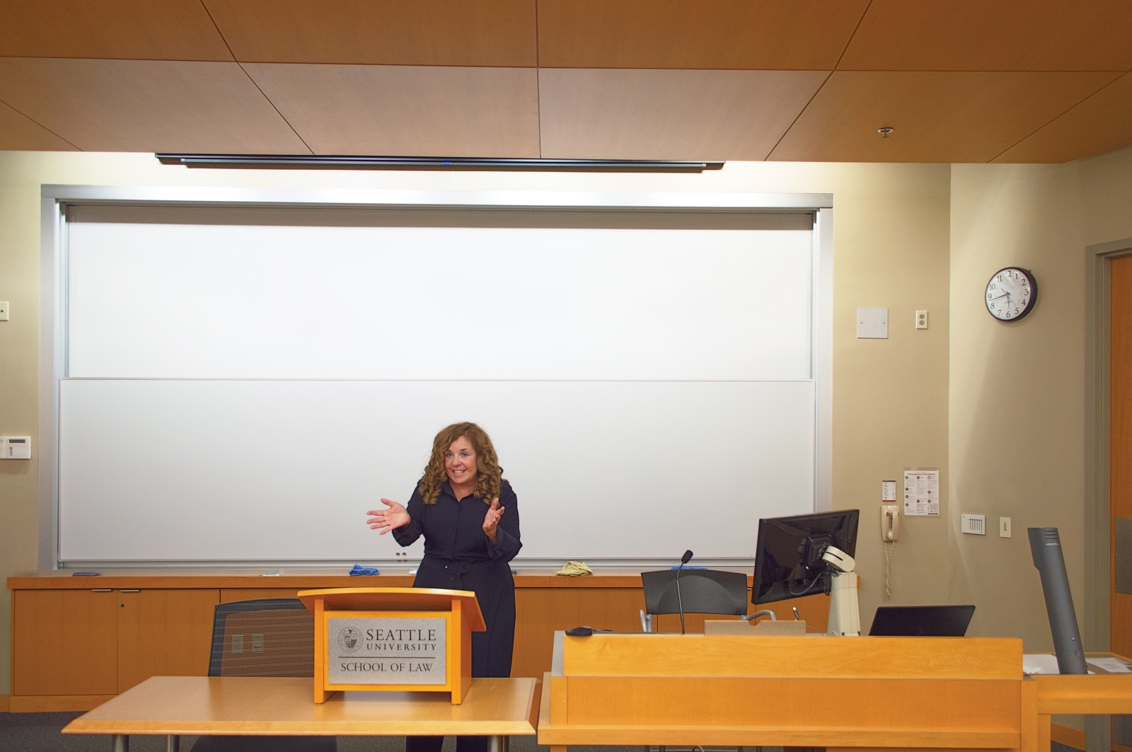 Woman in black blouse standing at a lectern in front of a classroom whiteboard