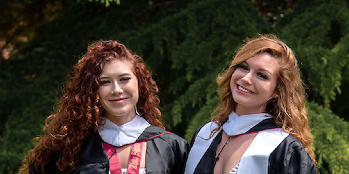 Eva and Amber standing side-by-side in graduation robes smiling