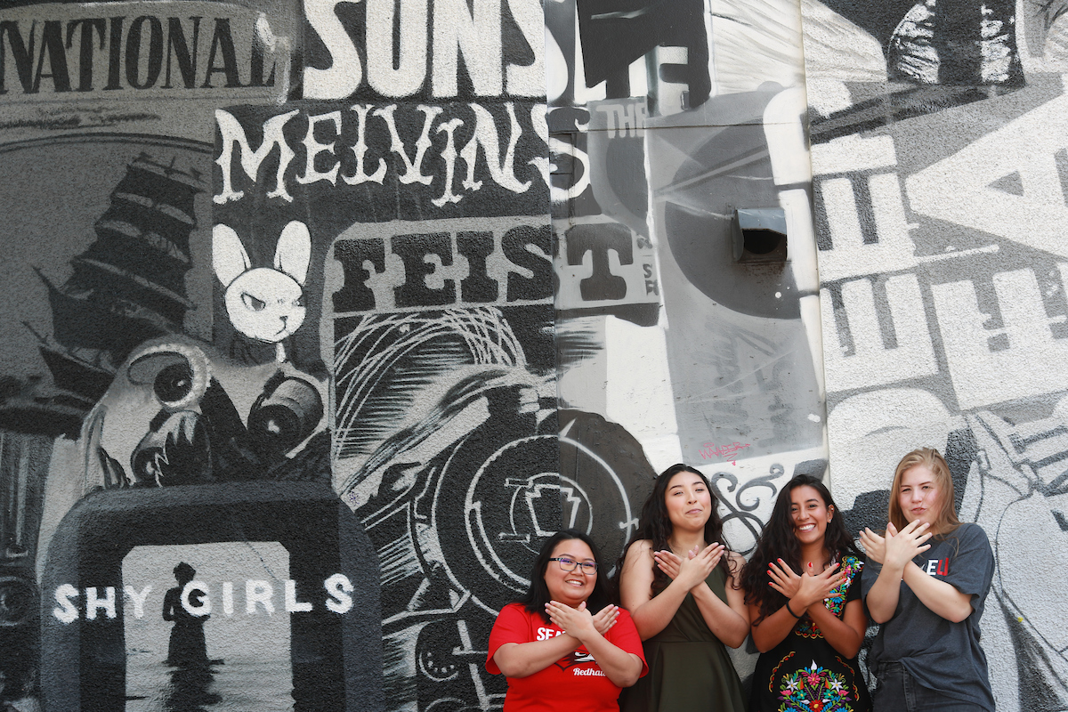 Four Seattle U students stand in front of a music-themed mural outside of Neumo's nightclub